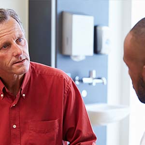 A man in a red button-up shirt discusses his health with his primary care doctor.